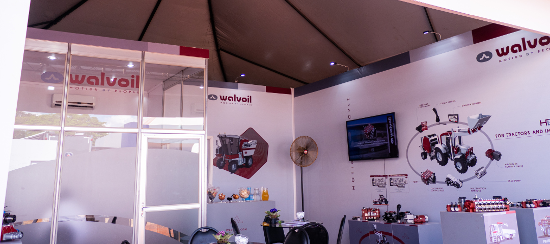 banner siteEstande da Walvoil com displays de produtos hidráulicos e ilustração de sistemas aplicados em tratores, durante a Agrishow 2024.